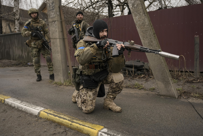 Un soldado ucraniano cubre la retirada de otros soldados que revisan cadáveres tirados en las calles en el suburbio Bucha, en Kiev Ucrania, el sábado 2 de abril de 2022.