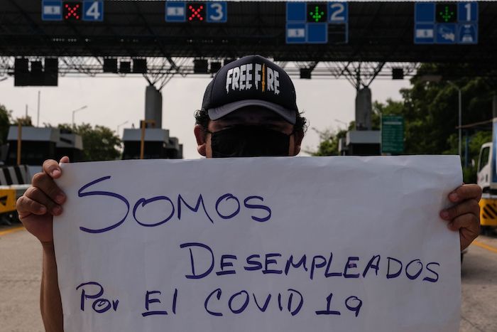 Un mesero desempleado muestra una pancarta a los conductores que pasan por la Caseta de Cobro de la carretera Tuxtla-San Cristóbal de las Casas, Chiapas, solicitando su apoyo.