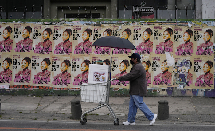 Un vendedor de empanadas empuja su carrito frente a los carteles de campaña de Francia Márquez, compañera de fórmula del candidato presidencial Gustavo Petro, de la coalición Pacto Histórico, en Bogotá, Colombia, el viernes 17 de junio de 2022.