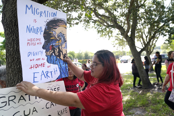 Cynthia Moreno, que se beneficia de un programa de alivio migratorio para jóvenes inmigrantes, cuelga un cartel frente a las Oficinas de Inmigración y Control de Aduanas en Miramar, Florida, el miércoles 15 de junio de 2022.