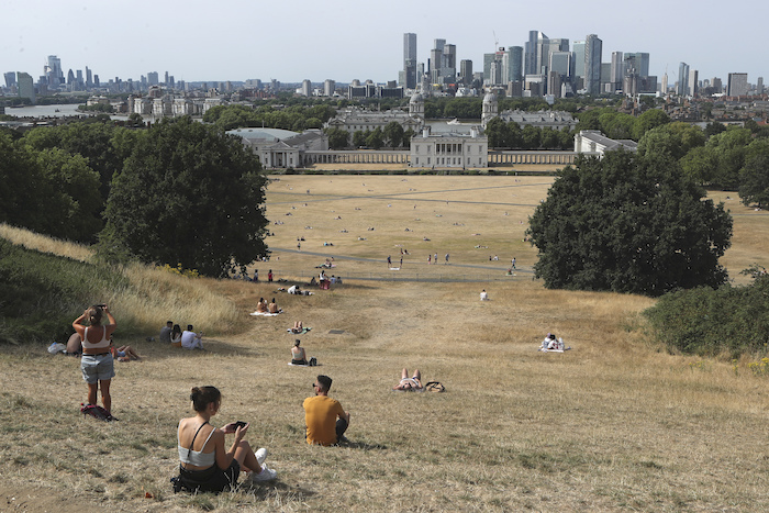 Gente Sentada En Pasto Seco Por El Sol En El Parque De Greenwich Con El Museo Marítimo Y El Distrito Financiero De Canary Wharf Al Fondo En Londres El Domingo De Julio De