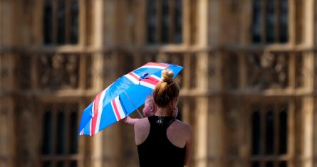 Una madre protege a su bebé del sol con un paraguas el martes 19 de julio de 2022, mientras camina por el puente de Westminster en Londres.