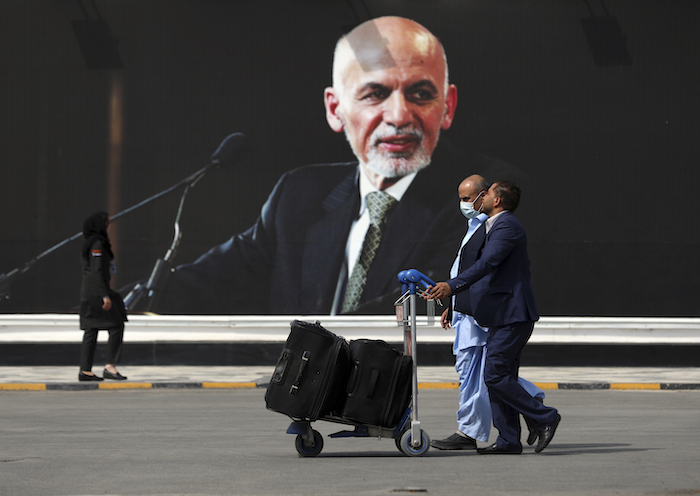 Pasajeros caminan hacia la terminal de salidas del Aeropuerto Internacional Hamid Karzai y pasan frente a una fotografía del Presidente Ashraf Ghani, el sábado 14 de agosto de 2021, en Kabul, Afganistán. 