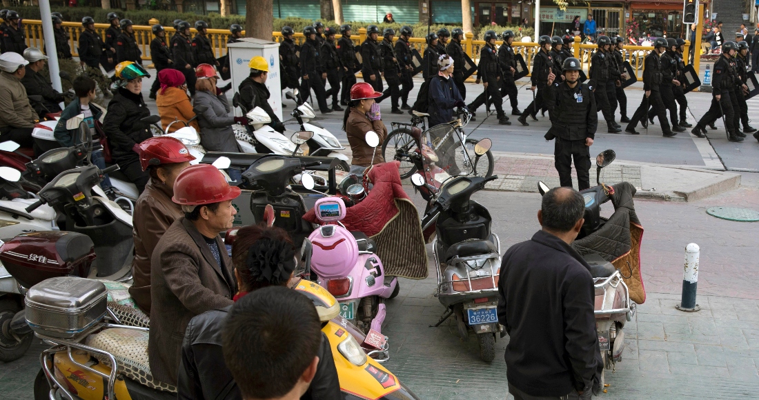 Residentes observan una caravana de personal de seguridad armado con toletes y escudos que patrulla el centro de Kashgar, el 5 de noviembre de 2017, en la región de Xinjiang, en el oeste de China.