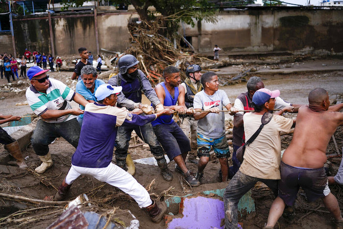 Los residentes locales y los trabajadores de socorro tiran de una cuerda para retirar los escombros en busca de sobrevivientes de una casa destruida por las inundaciones causadas por las fuertes lluvias en Las Tejerías, Venezuela, el domingo 9 de octubre de 2022.