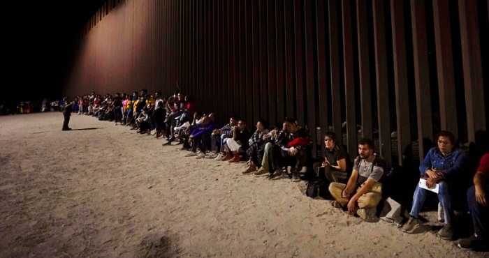 Migrantes esperan junto a un muro fronterizo el 23 de agosto del 2022, tras cruzar desde México cerca de Yuma, Arizona.