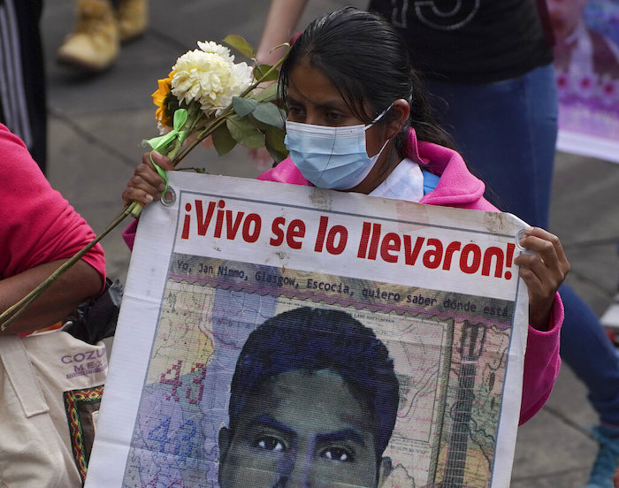 Un familiar de uno de los 43 estudiantes universitarios de Ayotzinapa desaparecidos marcha con un cartel que tiene la imagen de su ser querido y la frase "¡Vivo se lo llevaron!", en la Ciudad de México, el lunes 26 de septiembre de 2022, al cumplirse un nuevo aniversario de la desaparición de los estudiantes en Iguala, Guerrero, en 2014.