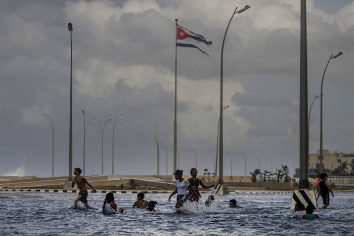 Una bandera cubana ondea en lo alto mientras chicos juegan en el mar frente al Malecón en La Habana, Cuba, el jueves 29 de septiembre de 2022.