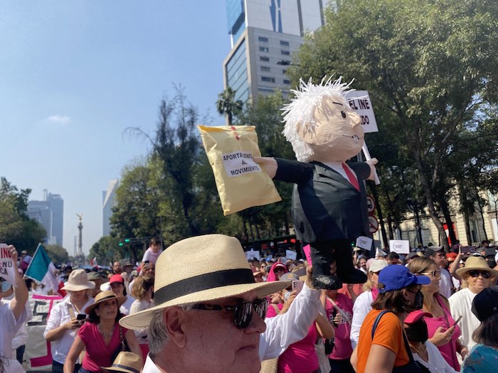 Claudio X. escucha las consignas a su espalda, poco antes de la Glorieta de la Palma, y pasa al lado de un monigote de cartón que representa a López Obrador, que en un brazo sostiene un sobre amarillo que dice: “Aportaciones al movimiento”.