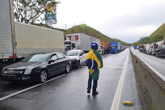 Un camionero con una bandera brasileña camina junto a camiones de carga detenidos en la carretera entre Río de Janeiro y Sao Paulo para protestar por la derrota electoral el día anterior del Presidente Jair Bolsonaro, el lunes 31 de octubre de 2022, en Barra Mansa, estado de Río de Janeiro, Brasil.