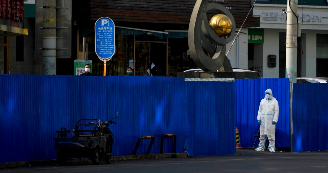 Un trabajador con equipo de protección observa al tiempo que residentes se congregan cerca de las barreras metálicas instaladas en torno a restaurantes que fueron cerrados como parte de los controles contra la COVID-19, en Beijing, el 10 de noviembre de 2022.