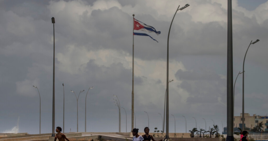 Una bandera cubana ondea en lo alto mientras chicos juegan en el mar frente al Malecón en La Habana, Cuba, el jueves 29 de septiembre de 2022.