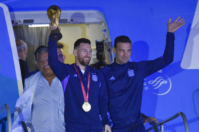 El futbolista argentino Lionel Messi sostiene el trofeo del Mundial de la FIFA a la salida de un avión junto al técnico Lionel Scaloni, en Buenos Aires, Argentina, el martes 20 de diciembre 2022.