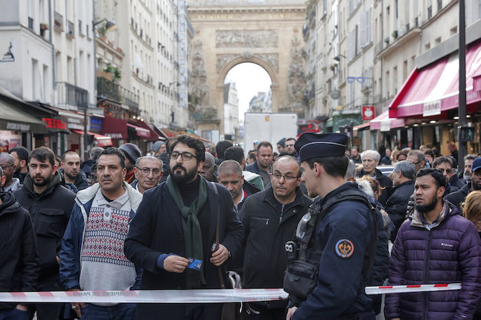 Transeúntes se agolpan detrás de la cinta que rodea la escena donde se produjo un tiroteo en el centro de París, viernes 23 de diciembre de 2022.