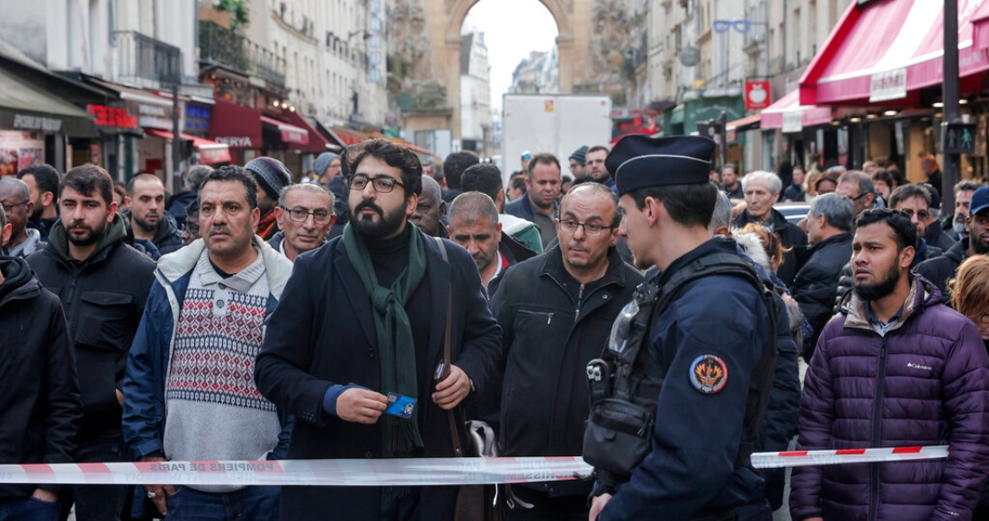 Transeúntes se agolpan detrás de la cinta que rodea la escena donde se produjo un tiroteo en el centro de París, viernes 23 de diciembre de 2022. El hecho dejó como saldo al menos dos muertos y cuatro heridos.