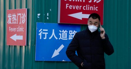 Un hombre con mascarilla habla por teléfono cerca de un cartel que dirige a los visitantes a una clínica para pacientes con fiebre en un hospital de Beijing, el sábado 10 de diciembre de 2022.