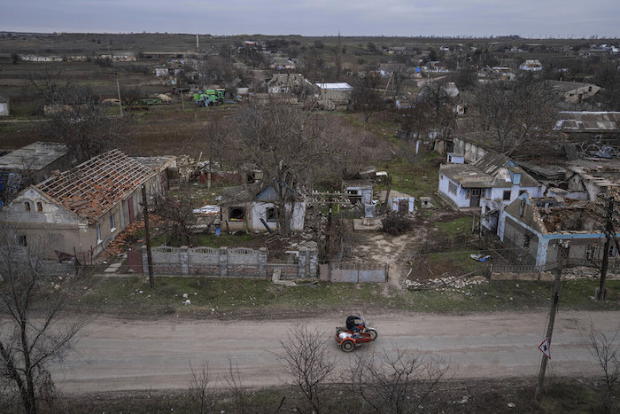 Un hombre pasa en motocicleta ante casas destruidas en los combates entre fuerzas rusas y ucranianas en la localidad recién liberada de Arhanhelske, Ucrania, el lunes 5 de diciembre de 2022.