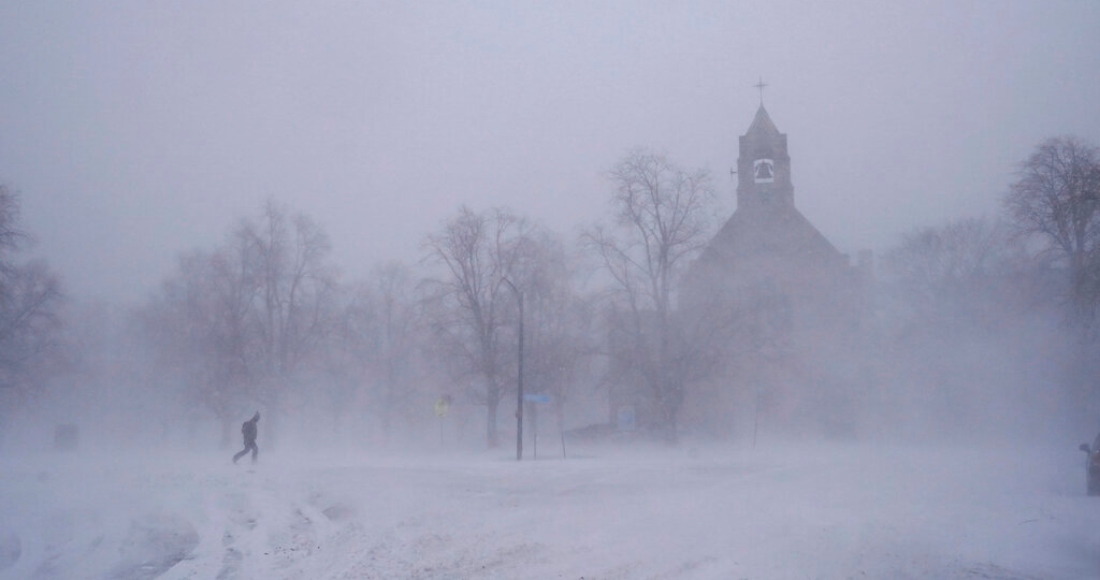 Un peatón con equipo para la nieve avanza por el Colonial Circle, con la silueta de la iglesia episcopaliana de St. John's Grace entre la ventisca, en Buffalo, Nueva York, el sábado 24 de diciembre de 2022.