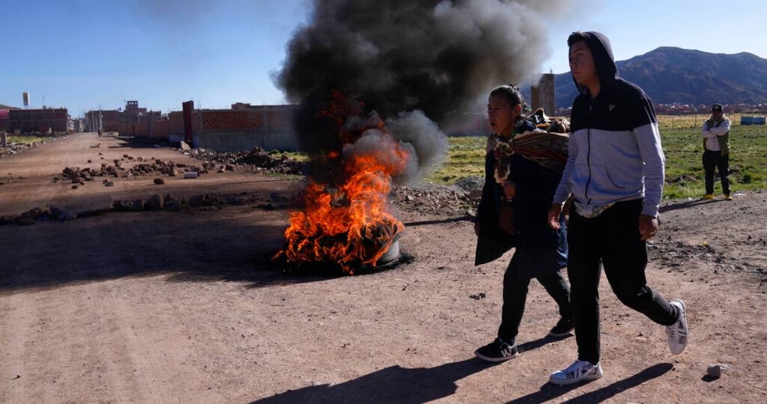 Los residentes pasan frente a un control de carreteras en llamas establecido por manifestantes antigubernamentales en Desaguadero, Perú, en la frontera con Bolivia, el viernes 13 de enero de 2023.