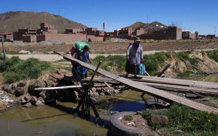 Mujeres pasan frente a los bloqueos de carreteras establecidos por manifestantes antigubernamentales para cruzar la frontera con Bolivia, en Desaguadero, Perú, el viernes 13 de enero de 2023. 