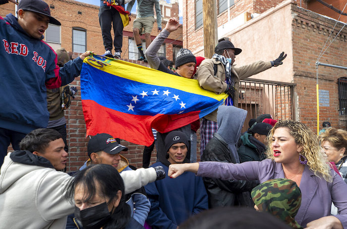 Un migrante de varios, a la izquierda, choca el puño con una residente local que los apoya en el centro de El Paso, Texas, el sábado 7 de enero de 2023. Al fondo varios migrantes muestran una bandera venezolana.