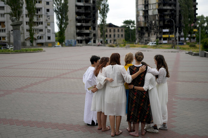 Jóvenes reunidos en un círculo mientras ensayan una representación cerca de un edificio dañado por ataques rusos en Borodyanka, a las afueras de Kiev, Ucrania, el martes 21 de junio de 2022.