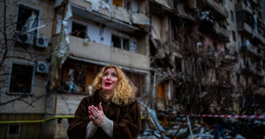 Natali Sevriukova se ve sobrepasada por la emoción, de pie ante su edificio de apartamentos destruido tras un ataque de cohete en Kiev, Ucrania, el viernes 25 de febrero de 2022.