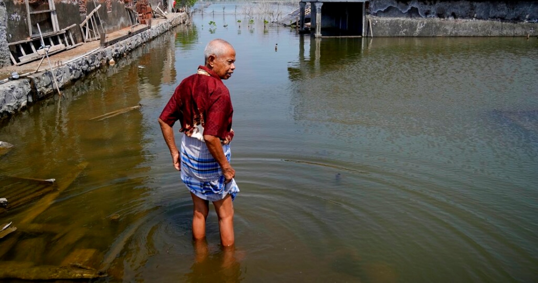 Sukarman camina por un camino inundado fuera de su casa el 30 de julio de 2022 en Timbulsloko, Java Central, Indonesia.