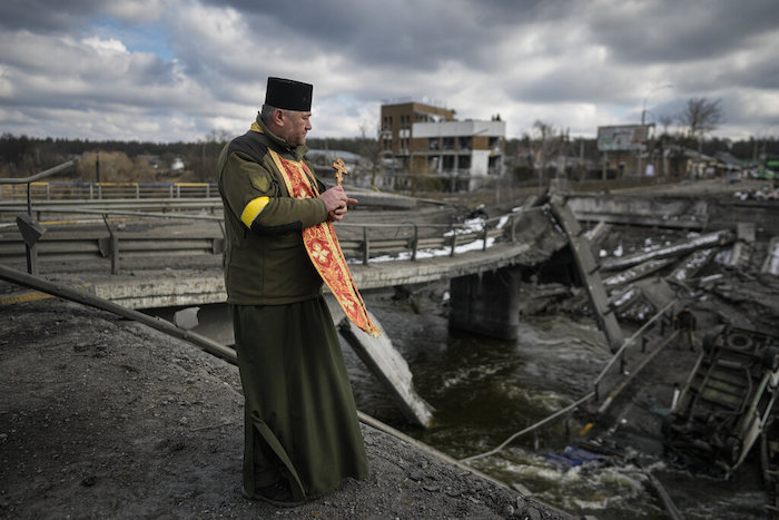 Un capellán militar ucraniano se ve de pie junto a un puente destruido en Irpin, a las afueras de Kiev, Ucrania, el miércoles 9 de marzo de 2022.