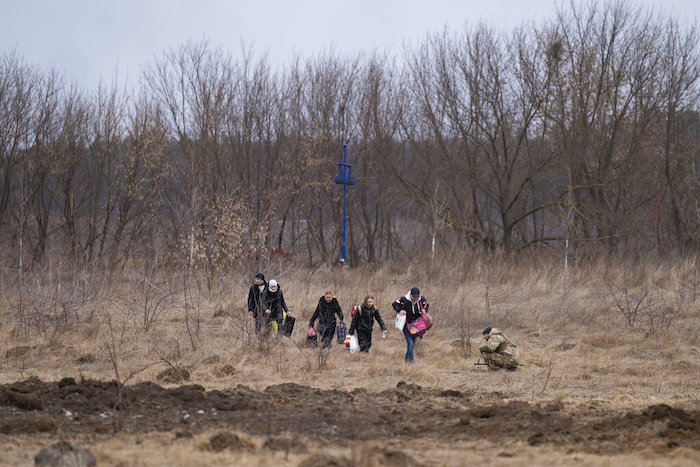 Mientras el ruido de la artillería suena cerca, un soldado ucraniano se agacha y varias personas huyen de Irpin, a las afueras de Kiev, Ucrania, el lunes 7 de marzo de 2022.