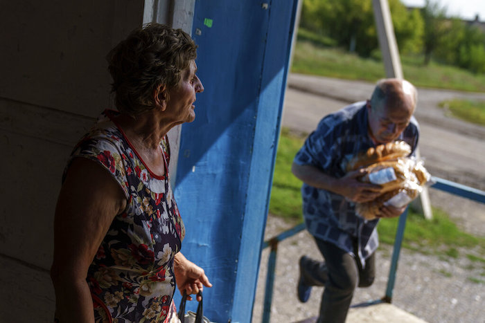 Vasyl Moiseienko, un jubilado, lleva pan fresco mientras una anciana espera la entrega en un comercio de Dyliivka, en la región de Donetsk, en el este de Ucrania, el sábado 20 de agosto de 2022.