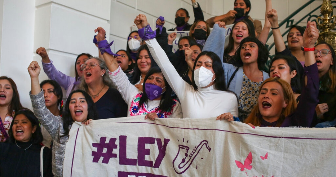 La sobreviviente de ataques con ácido, María Elena Ríos, al centro y con una mascarilla blanca, y Elisa Xolalpa, al centro izquierda, levantan los puños al unísono durante una conferencia de prensa sobre un proyecto de Ley que lleva el apodo de Ríos, "Malena", en el Congreso de la Ciudad de México, el martes 31 de enero de 2023.