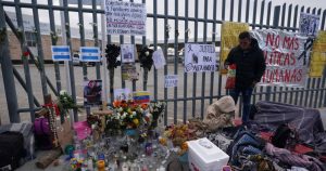 Un altar con velas y fotos cubre la cerca afuera del centro de detención de migrantes que fue el sitio de un incendio mortal, mientras los migrantes se despiertan después de pasar la noche en la acera en Ciudad Juárez, México, el jueves 30 de marzo de 2023.