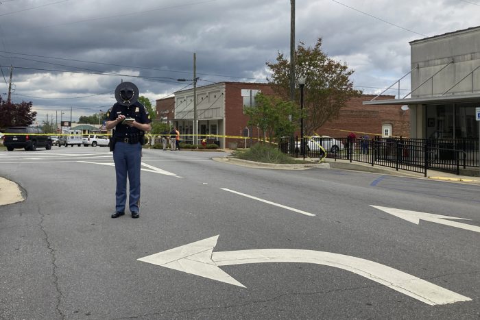 Un policía de Alabama revisa su teléfono mientras los investigadores trabajan en el lugar de un tiroteo fatal en el centro de Dadeville, Alabama, el domingo 16 de abril de 2023.