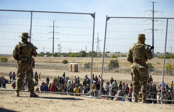 Migrantes esperan junto a una valla fronteriza mientras son vigilados por miembros de la Guardia Nacional de Texas, para ingresar a El Paso, Texas, el miércoles 10 de mayo de 2023.