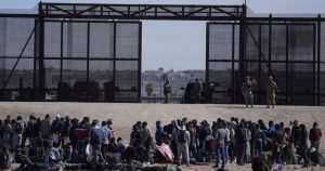 Migrantes que cruzaron la frontera desde México hacia Estados Unidos esperan a un costado del muro fronterizo en donde agentes de la Patrulla Fronteriza de Estados Unidos montan guardia, el 30 de marzo de 2023, en una imagen tomada desde Cuidad Juárez, México.