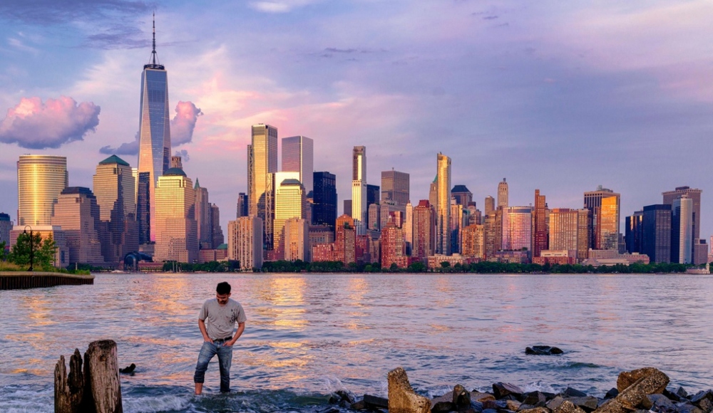 Un hombre comprueba dónde pisa mientras camina por el agua en el Canal Morris en Jersey, Nueva Jersey, mientras se pone el sol con Manhattan de fondo, el 31 de mayo de 2022. Foto: J. David Ake, Archivo, AP