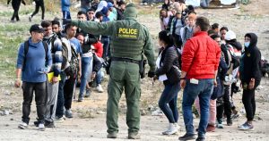 Un agente de la Patrulla Fronteriza da indicaciones a solicitantes de asilo para que esperen en la frontera de Estados Unidos con México, cerca de Tijuana, México, el lunes 8 de mayo de 2023, en San Diego.