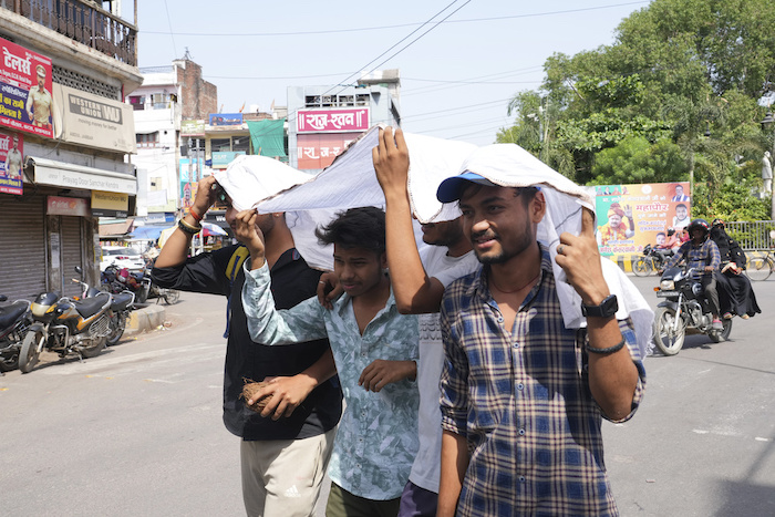 Jóvenes compartiendo un trozo de tela para protegerse del sol en un día caluroso de verano en Prayagraj, en el estado norteño de Uttar Pradesh, India, el domingo 21 de mayo de 2023.