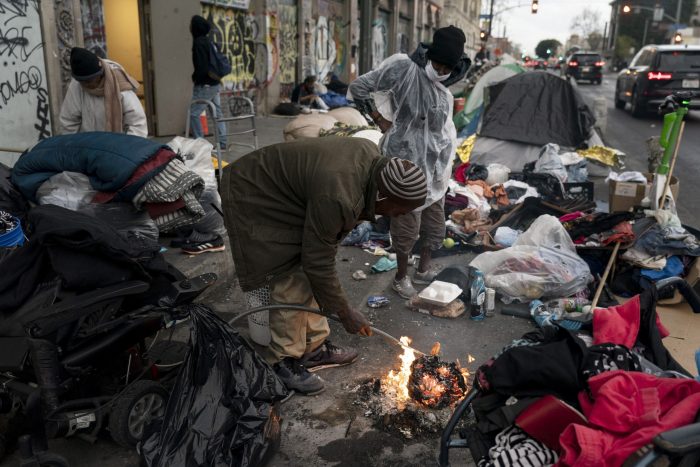 Robert Mason, un vagabundo de 56 años, calienta un trozo de alimento en una fogata que prendió para mantenerse caliente en la zona Skid Row de Los Ángeles, el 14 de febrero de 2023.