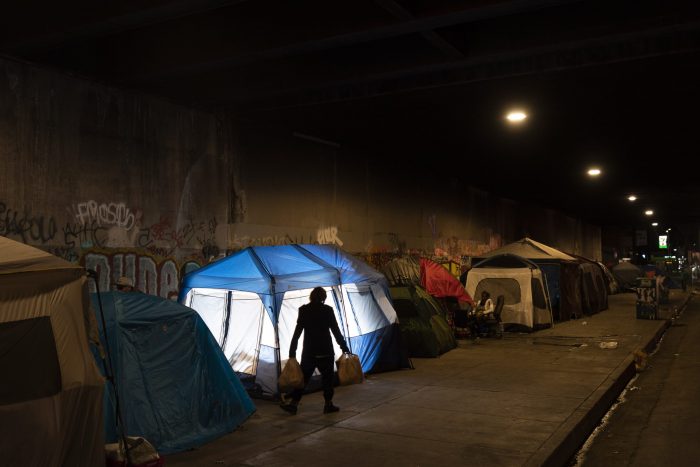 Un hombre camina junto a un campamento de indigentes instalado debajo de un puente en Los Ángeles, el 9 de febrero de 2023. La tienda de campaña azul fue iluminada desde el interior mediante un flash externo.