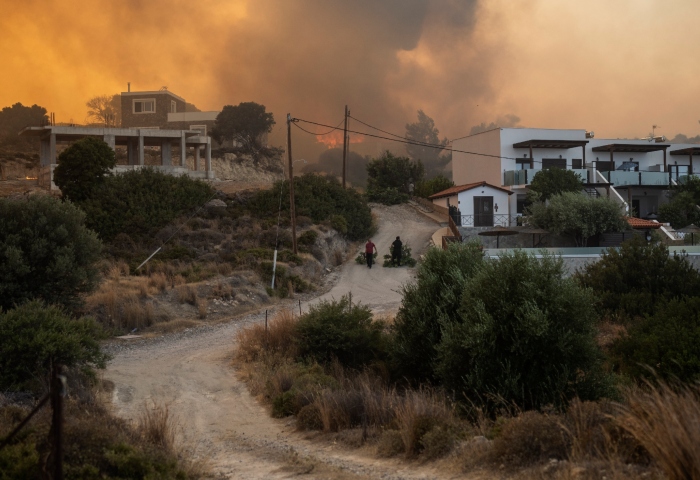 Residentes arrastran ramas de árboles mientras un incendio arde en las inmediaciones de Gennadi, en la isla de Rodas, en el sureste de Grecia, el 25 de julio de 2023. Foto: Petros Giannakouris, AP