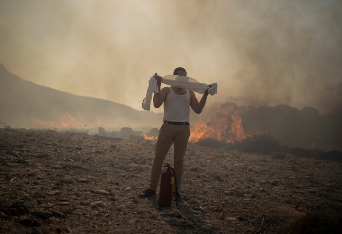 Un hombre se tapa el rostro con su camisa mientras trata de extinguir un incendio cerca del balneario costero de Lindos, en la isla de Rodas, en el sureste de Grecia, el 24 de julio de 2023. Foto: Petros Giannakouris, AP