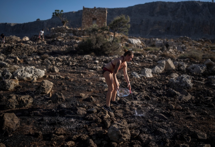 Jaquelin Stocklein, de Alemania, arroja agua en una zona arrasada por un incendio cerca del balneario costero de Lindos, en la isla de Rodas, en el sureste de Grecia, el 24 de julio de 2023. Foto: Petros Giannakouris, AP