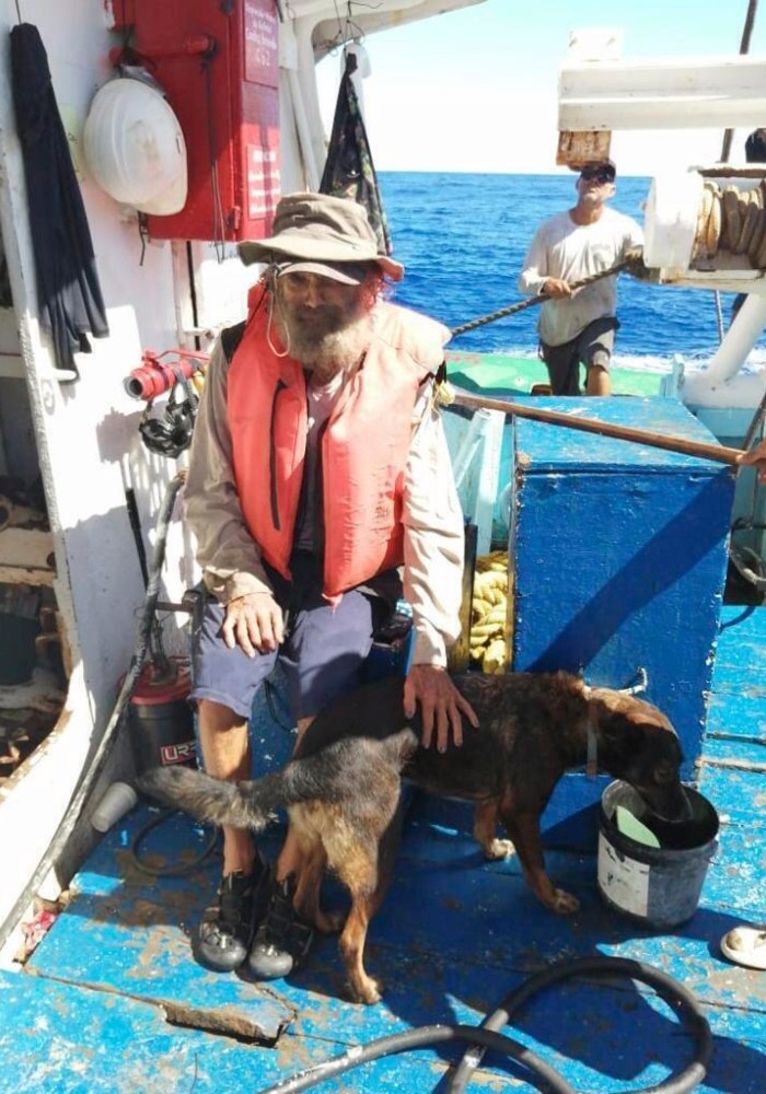 En esta fotografía proporcionada por Grupomar/Atun Tuny, el australiano Tim Shaddock permanece sentado con su perra Bella tras ser rescatado por un buque atunero mexicano en aguas internacionales del Pacífico, luego de que navegó a la deriva con Bella en su catamarán averiado durante tres meses. Foto: Grupomar, Atun Tuny vía AP