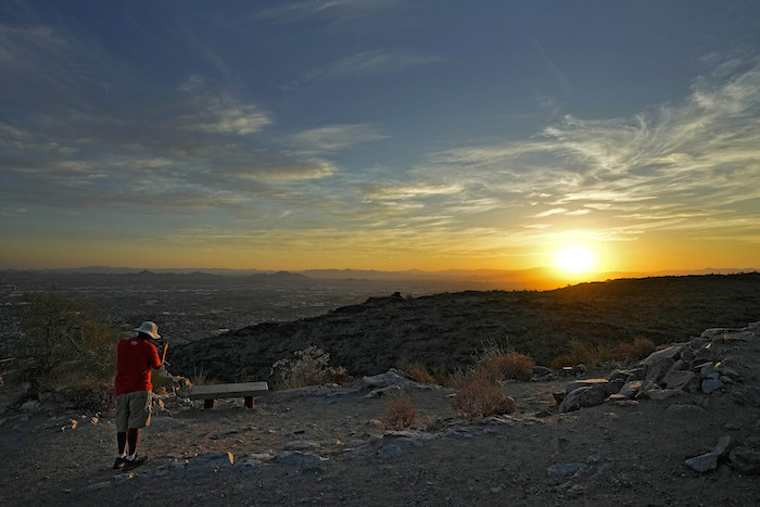 Un excursionista fotografía la salida del sol el lunes 17 de julio de 2023, sobre el valle que domina la cima de South Mountain, en Phoenix.