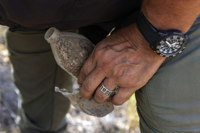 El investigador del condado Jim Hogg Ruben Garza sostiene botellas de agua vacías mientras investiga la desaparición de un puesto de hidratación para migrantes, que contenía garrafas cerradas de agua, junto a una carretera en una zona rural del condado Jim Hogg, Texas, el martes 25 de julio de 2023. 