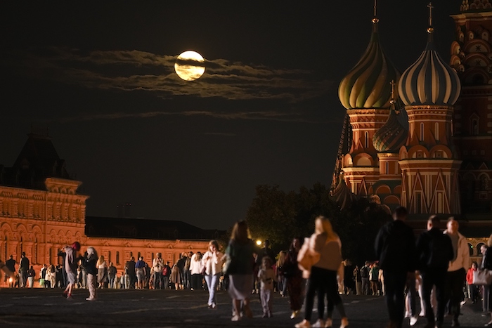 La súperluna azul de agosto detrás de un edificio histórico y la Catedral de San Basilio a la derecha, mientras la gente camina en la Plaza Roja de Moscú, Rusia, el miércoles 30 de agosto de 2023.