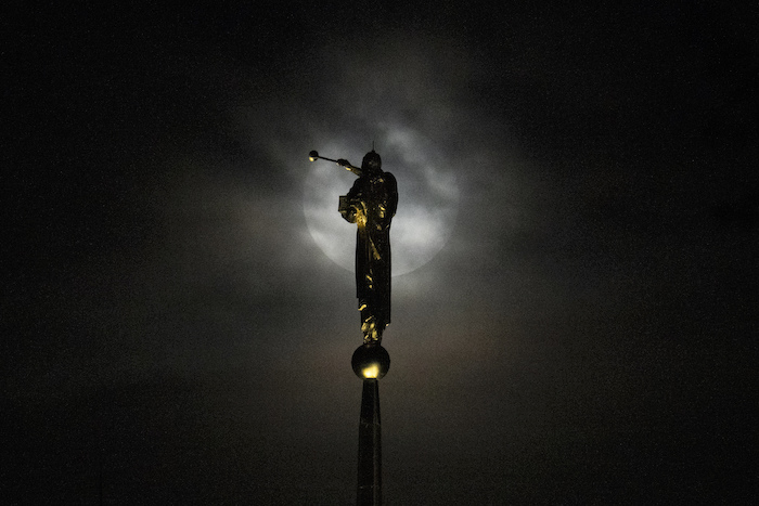 La súperluna se deja ver detrás de una densa capa de nubes cerca de una estatua del ángel de Moroni, en lo alto de la Iglesia de Jesucristo de los Últimos Días, en Kensington, Maryland, el 30 de agosto de 2023.