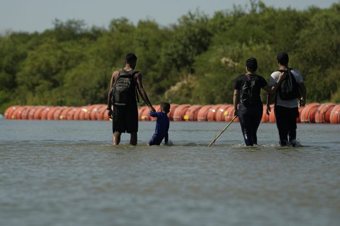 Migrantes en su ruta hacia Estados Unidos desde México camina a lo largo de las boyas instaladas como una barrera flotante sobre el Río Bravo, el martes 1 de agosto de 2023, en Eagle Pass, Texas.